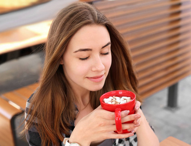 美丽的年轻妇女与杯子甜可可饮料在咖啡馆