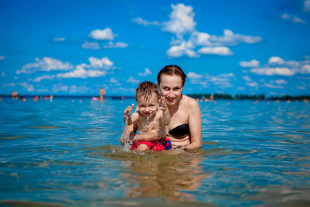 年轻的妈妈带着一个小男孩在湖边玩水, 在夏天, 家庭幸福, 乡村家庭休息, 夏天温暖的日子, 幸福
