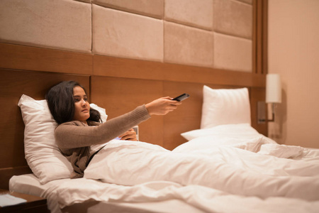晚上在床上的女人看电视和手持电视遥控器