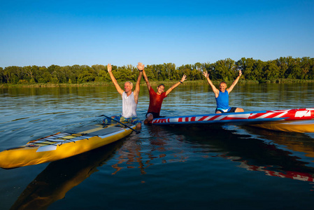 快乐的朋友们, 在日落的时候, 一只张开双臂的冲浪者在大河上放松, 玩得开心。站起来桨登机可怕的主动户外娱乐
