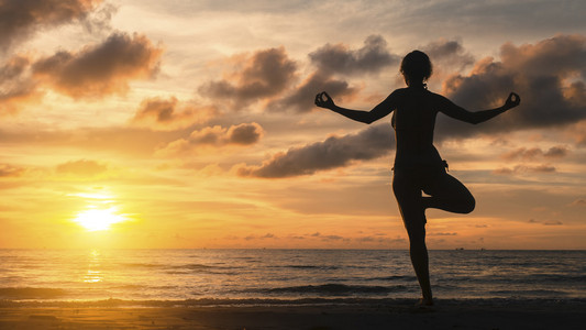 在日落时分做瑜伽在海滩上的女人