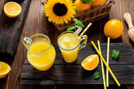 一杯鲜榨的橙汁, 上面放着冰块和橘子在木桌上。秋天舒适质朴的心境静物