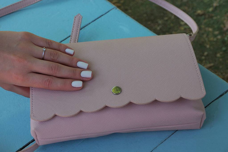 女孩的手指躺在蓝色桌子上的粉红色钱包上