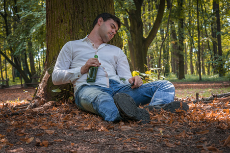醉酒的男子躺在地上，在树下的啤酒瓶