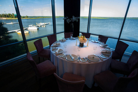圆形宴会桌上配有餐具, 装饰着蜡烛和鲜花, 背景是豪华餐厅的海和游艇。