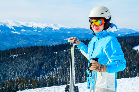 穿着蓝色西装的女人, 头盔和眼镜站在山顶上的滑雪板上。