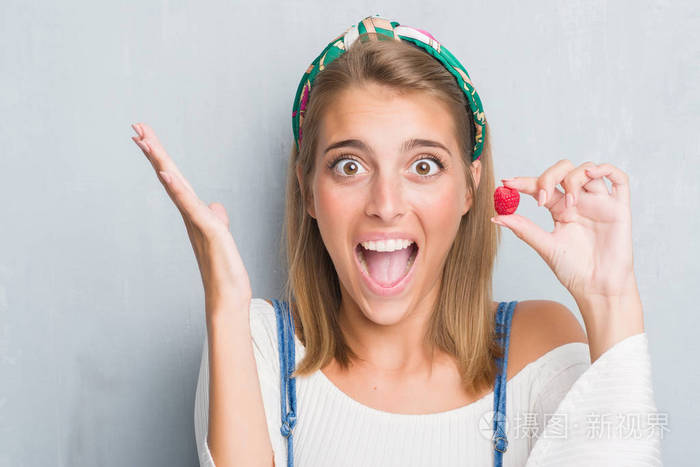 美丽的年轻女人在灰墙上吃新鲜的覆盆子非常高兴和兴奋, 优胜者表达