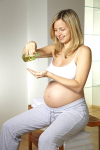金发孕妇穿着白色内衣浇注身体油按摩她的肚子在浴室