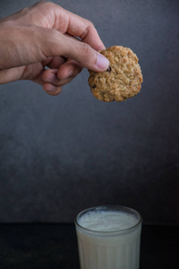 美味的燕麦饼干在手。黑暗的背景。在一张桌子上一杯白牛奶