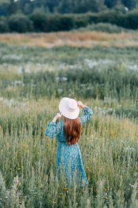 美丽的俄罗斯女孩在帽子和夏季礼服, 走在田野上的草地上的腰部。快乐的旅行者, 收集草药, 微笑。森林中的日落