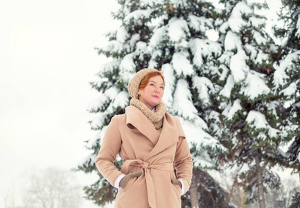 快乐的女人在冬天的时候。一个冬天的妇女在户外对绿色松树的背景下的雪