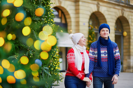 快乐的情侣在五颜六色的毛衣走在巴黎的街道装饰圣诞节
