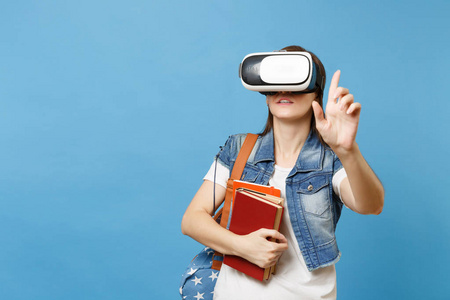 在虚拟现实护目镜的年轻女子的学生举行书籍触摸像按按钮, 指向在蓝色背景上孤立的浮动虚拟屏幕。学校大学教育