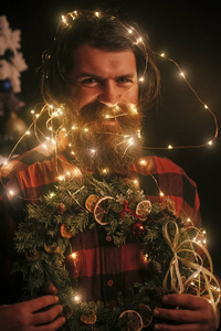 党和庆祝。寒假和圣诞节。带照明线的新年人。圣诞男子与胡子幸福的脸和花环。花环在圣诞老人人作为装饰举行花圈