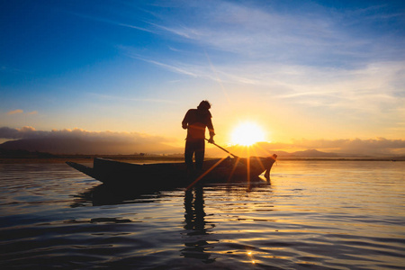 剪影渔夫站立在小船在日出期间