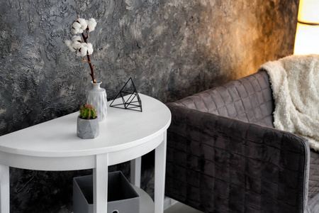 在黑墙附近的花瓶和沙发上放有棉花花枝的桌子