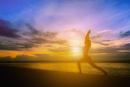 剪影年轻女子在日落时练瑜伽在海滩上