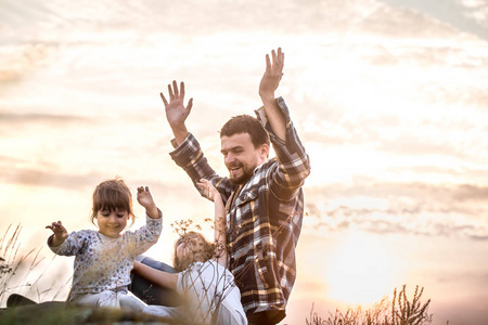 幸福美满的家庭, 爸爸和两个小可爱的女儿在日落时坐在一座高高的美丽