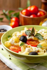 面食沙拉与樱桃西红柿, 黑橄榄, 羊乳酪和罗勒在木质背景。选择性聚焦