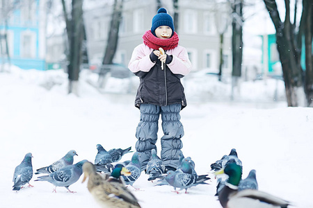 小女孩在冬季公园喂鸟, 关爱的概念, 家庭, 步行。慷慨大方的孩子用面包对待鸽子。服装, 季节性, 温暖, 运动