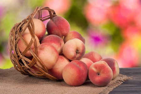在模糊的背景与木制的桌子上的柳条篮子里的桃子照片