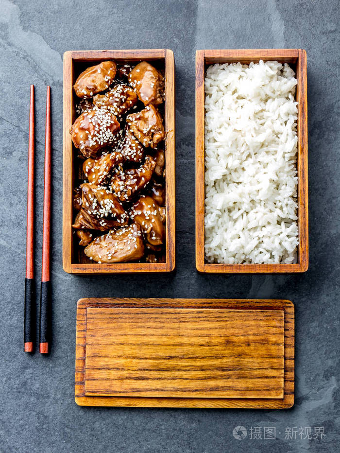鸡肉在木制便当饭盒里用米饭烧.石板背景, 顶部视图