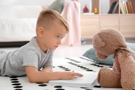 可爱的小男孩与泰迪熊读书在地板在家