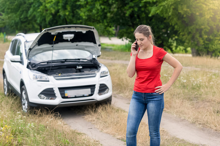 女人站在乡村道路上的破车，并呼吁 cellph