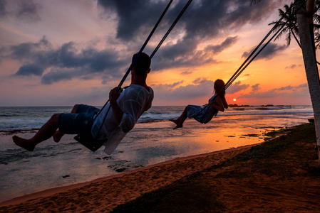夕阳背影男一对情侣剪影的背影, 坐在秋千上, 看着太阳在温暖的背景下