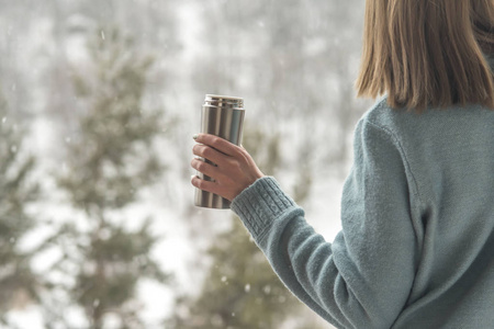 妇女在冬天森林的背景在一个热水瓶在手