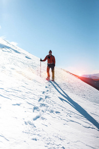 一个人爬上山顶。登山运动员在雪地鞋背着一个背包。在冬天的山上旅行。大自然中的极端假期。极端条件下的旅游者