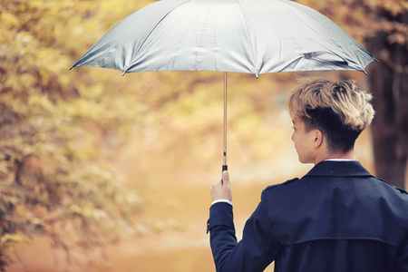 秋天公园在阴雨天气和一个年轻人用雨伞