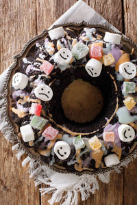 有趣的黑庞德蛋糕与蜜饯水果, 棉花糖和五颜六色的釉面上的桌子上。从 abov 垂直顶部视图