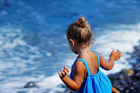 在希腊圣托里尼的 Paradisos 海滩上玩蓝色连衣裙的小女孩
