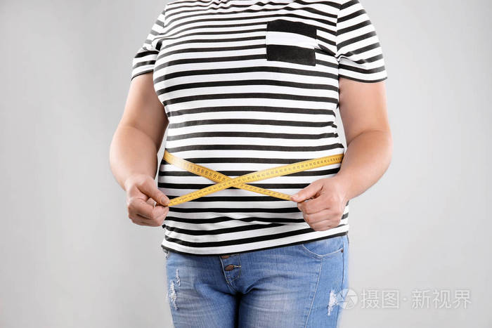 胖女人用卷尺在灰色背景, 特写。减肥