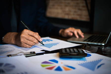 一个会计人员拿着钢笔, 用计算器在办公室的木桌上做公司税.