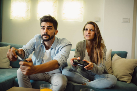 年轻夫妇的肖像玩视频游戏, 而坐在沙发上的家