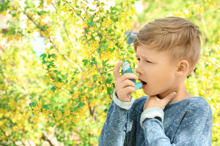 小男孩使用吸入器附近开花树。过敏概念