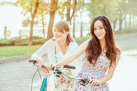 两个年轻女孩与在公园里骑自行车