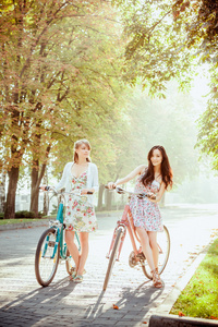 两个年轻女孩与在公园里骑自行车