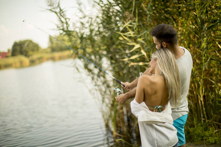 可爱的年轻夫妇一起在夏天的湖泊一起钓鱼
