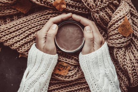 针织围巾和秋叶背景下女性手上的暖可可杯