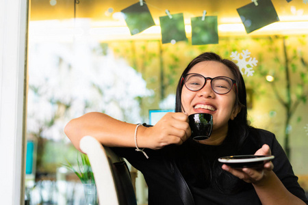 有眼眼镜的亚洲女人微笑着喝咖啡在咖啡馆里