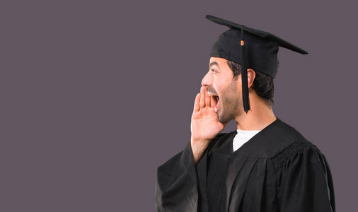 男子在他的毕业日大学大喊与嘴宽开放的横向和宣布的东西在紫罗兰背景