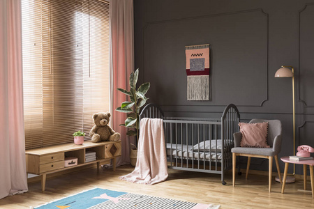 毛绒玩具在木柜子旁边的灰色摇篮在儿童的粉彩卧室内饰。真实照片