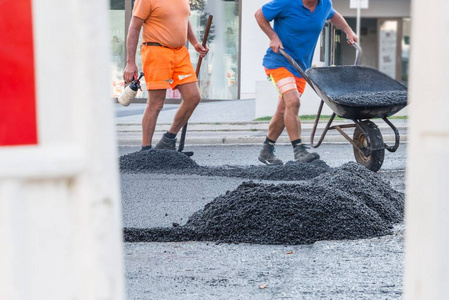 公路工人用铲子和手推车在公路上分发热沥青, 德国