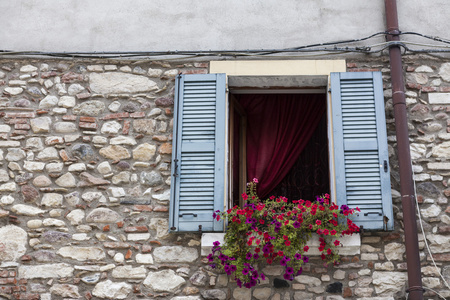 与旧窗口百叶窗打开石头墙上窗台上的花。意大利村