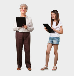 整个身体的老太太和她的孙女微笑和自信, 手持平板电脑, 利用它上网冲浪, 看到社交网络, 沟通的概念