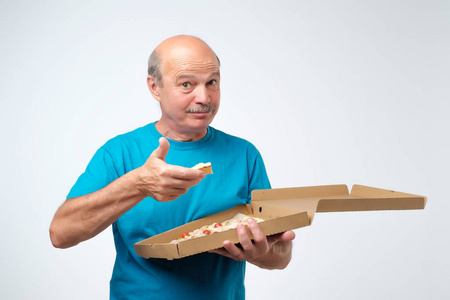 一个成熟的欧洲男人的肖像吃一块比萨饼。他手里拿着一盒食物。工作室拍摄。老年吃快餐的概念