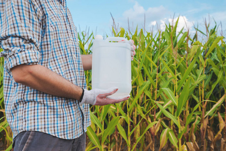 农夫在玉米地里持有农药化学水罐。空白无标号瓶作为模拟的复制空间的除草剂, 杀菌剂或杀虫剂用于玉米作物耕作